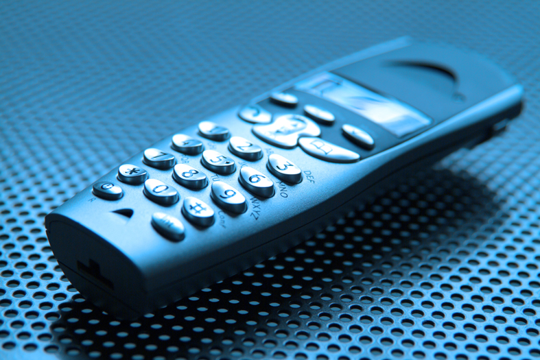 fotografia em tons de azul de um telefone do tipo "sem fio" repousado sobre base texturizada.