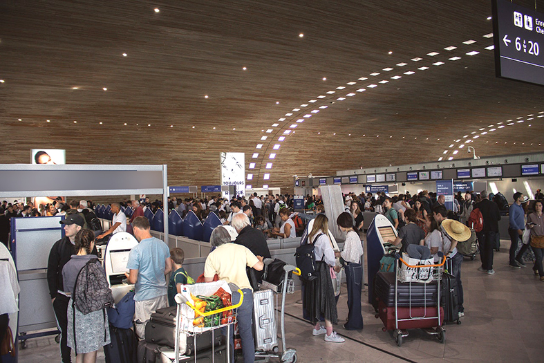 Saguão de um grande aeroporto, muitos passageiros circulando com malas e carrinhos.