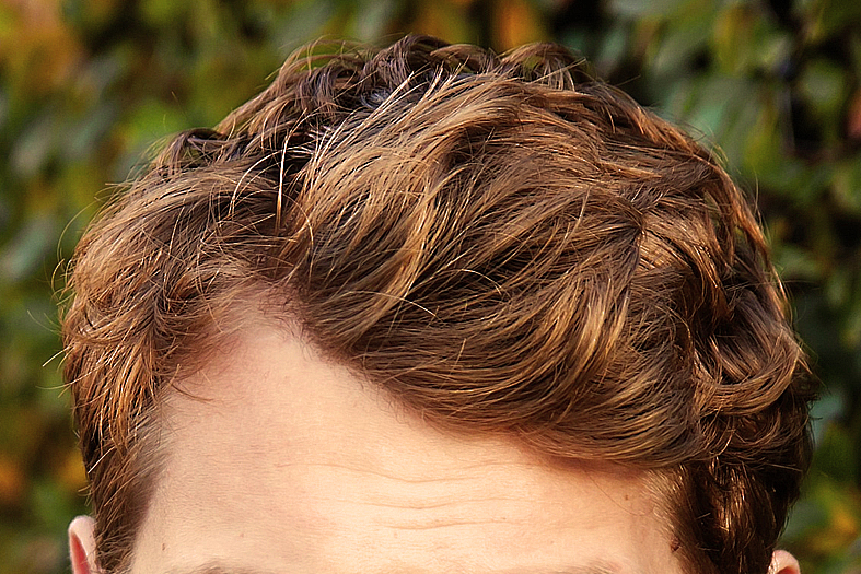 detalhe do penteado de um homem de pele branca e cabelos tingidos em tom cobre.
