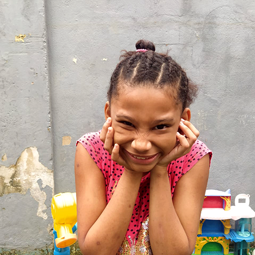 jice, 11 anos, com as mãos no queixo. ao fundo alguns brinquedos