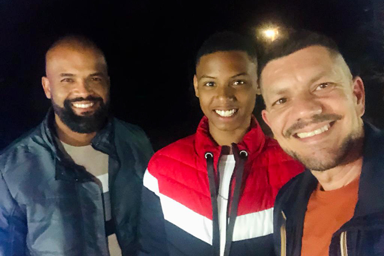 Dois homens e um adolescente sorriem para a câmera.
