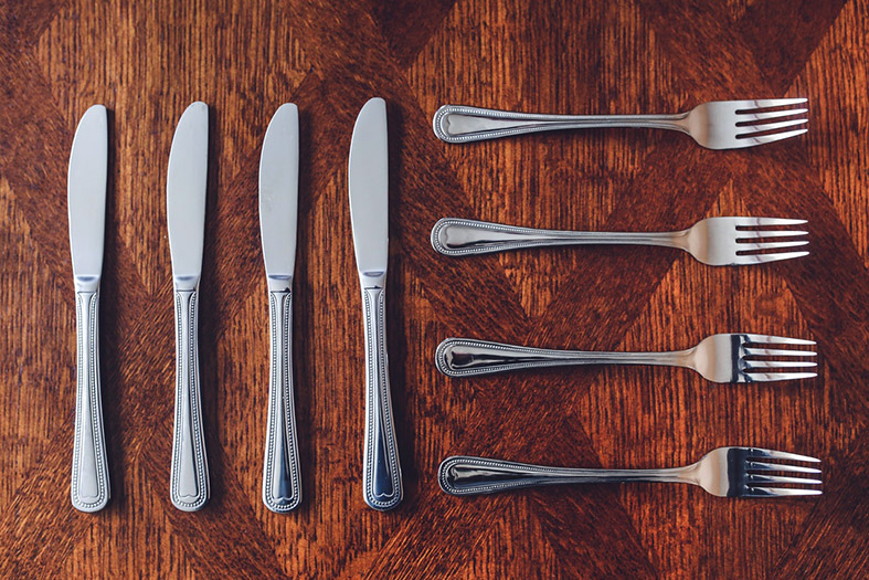 Três facas e três garfos alinhados em uma mesa de madeira.