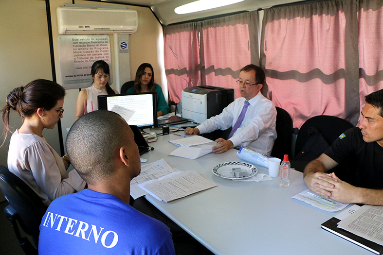 Pessoas sentadas ao redor de uma mesa no interior de um ônibus adaptado para escritório.