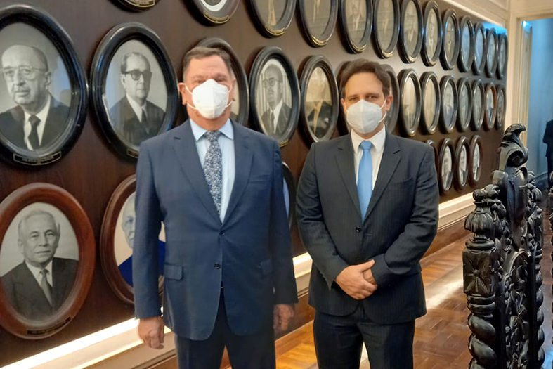 O presidente do TJES, Desembargador Ronaldo Gonçalves e o Juiz Auxiliar da Presidência, Dr. Thiago Albani posam para foto em frente a galeria de ex-presidentes do TJPE. Ambos usam terno e estão de máscara.