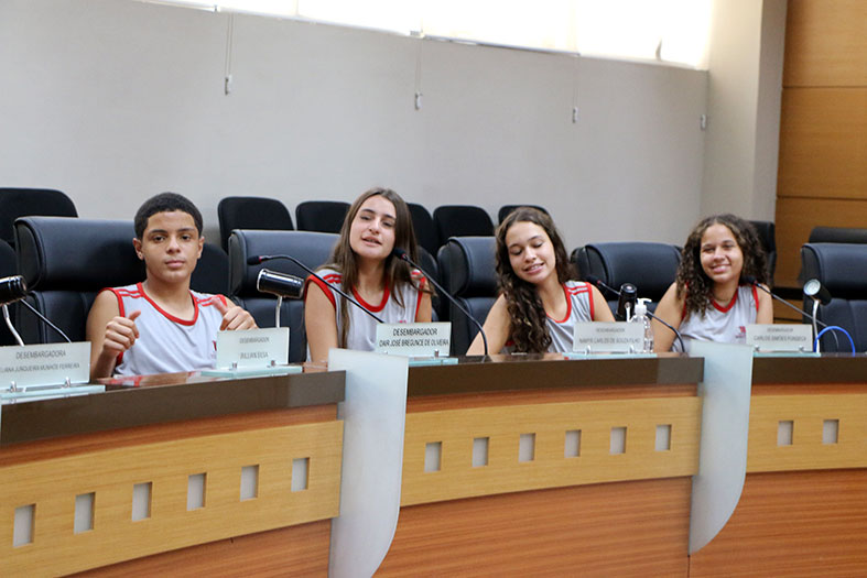 Quatro alunos da Escola Mundo Livre (Serra/ES) posam para foto nas bancadas ocupadas pelos desembargadores no salão do Tribunal Pleno do TJES.