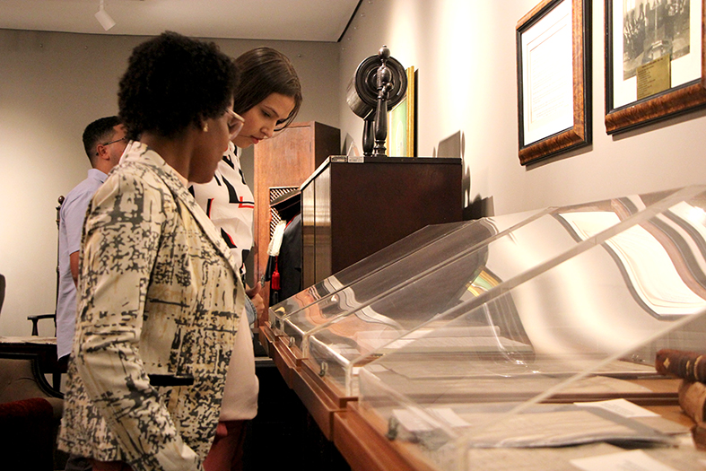 Duas mulheres observam um documento histórico dentro de um mostruário de acrílico.