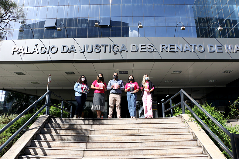 Cinco pessoas, quatro mulheres e um homem posam para foto ao final da escadaria que leva à entrada da sede do TJES.