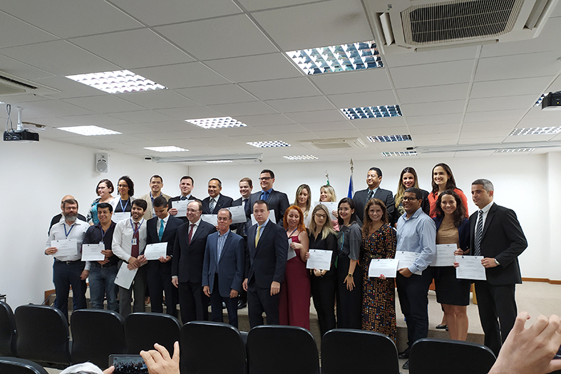 Grupo de pessoas posa para foto em um auditório. todas seguram certificados em suas mãos.