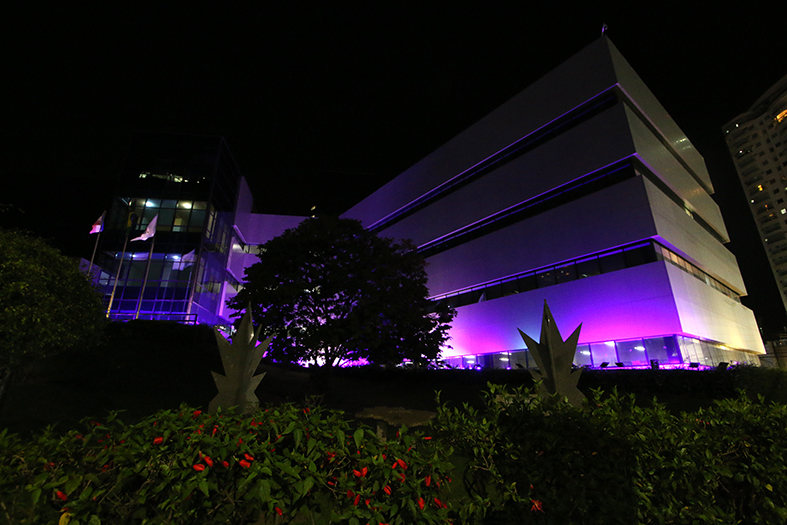 Foto noturna da fachada da sede do Tribunal de Justiça iluminado com luzes em tons de roxo.