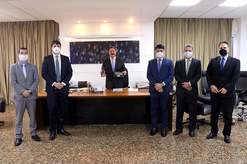 presidente do tjes, desembargador ronaldo gonçalves de sousa segurando u=em suas mãos um cartão e uma escultura com o formato do território do estado do espírito santo. afastados, posicionados mais à frente estão quatro membros do sinoreg. além do dr. thiago albani, juiz acessor especial da presidência do tjes.
