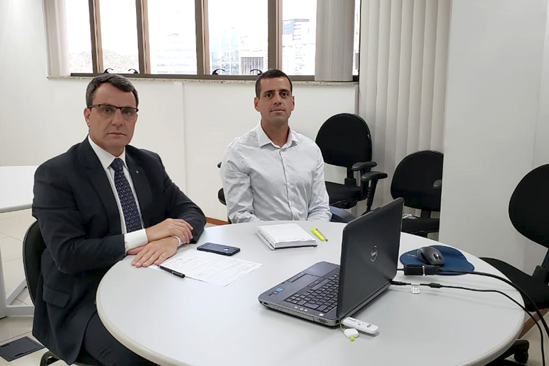 Duas pessoas sentada em torno de uma mesa redonda com documentos e notebooks dispostos sobre a mesa.