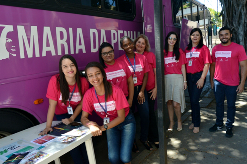Voluntários posam em frente a ônibus de cor rosada.