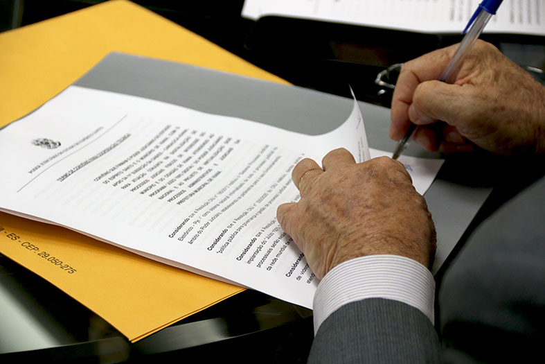 Detalhe de homem assinando um documento.