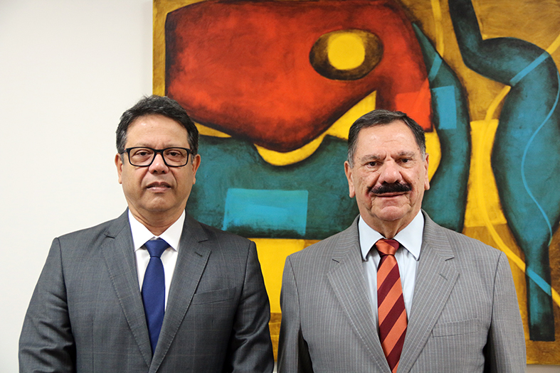 O presidente do TJES, desembargador Ronaldo Gonçalves e o procurador geral da Justiça, Eder Pontes posam para foto, ao fundo um quadro abstrato colorido.