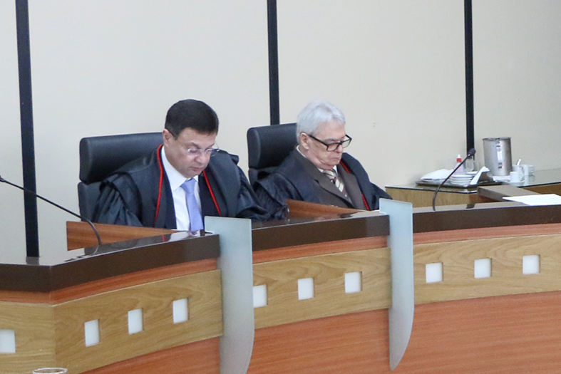 Dois desembargadores homens em mesa na sala de sessões.