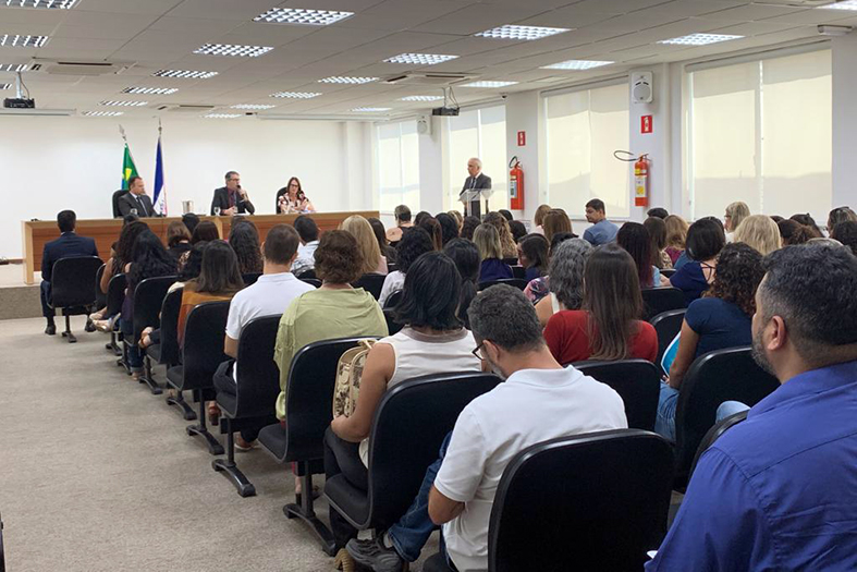 EM um auditório lotado pessoas assistem a palestra de duas pessoas.