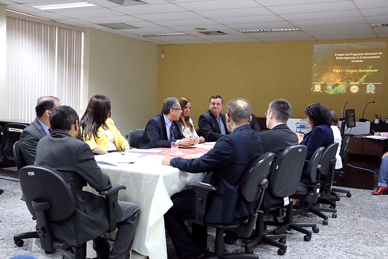 Grupo de pessoas reunidas entorno de uma mesa observando uma projeção na parede