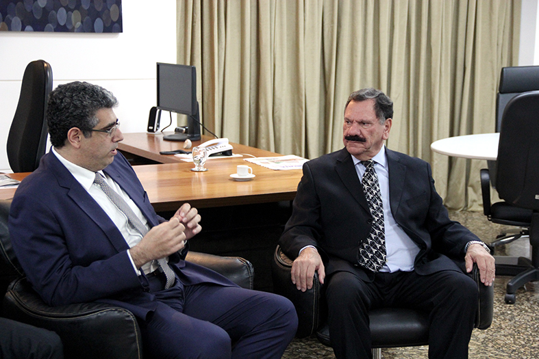 Dois homens de terno conversam em um gabinete.