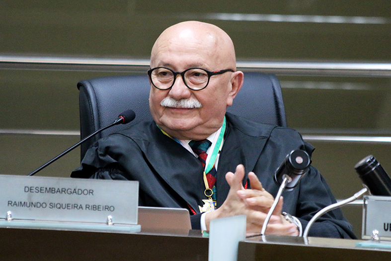 O desembargador Raimundo Siqueira Ribeiro, homem de pele branca, calvo, com bigode na cor branca. Ele usa óculos de grau de armação na cor preta e beca.