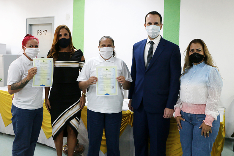 autoridades e reeducandas do sistema prisional de cachoeiro de itapemirim posam para foto. as reeducandas seguram as certidões de nascimento de seus filhos.