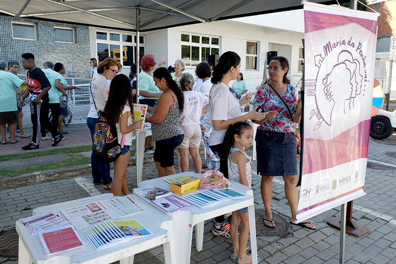 Grupo de pessoas conversando em um ambiente externo próximos à mesas onde se estão dispostos panfletos e brochuras.