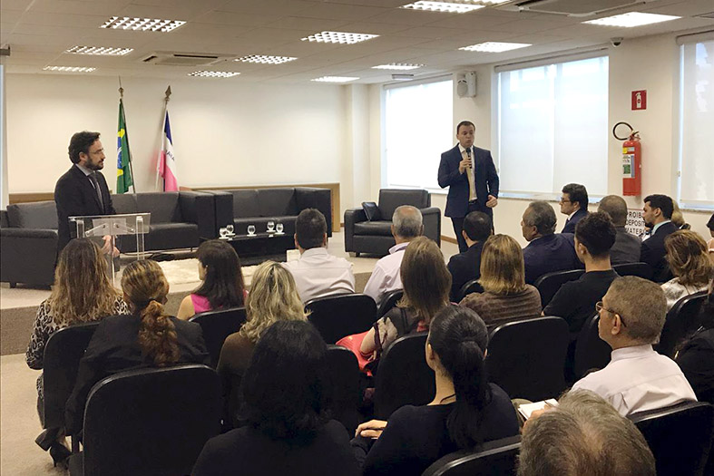 Auditório da Escola da Magistratura do ES. Pessoas assistindo o coordenador acadêmico da escola apresentando o evento