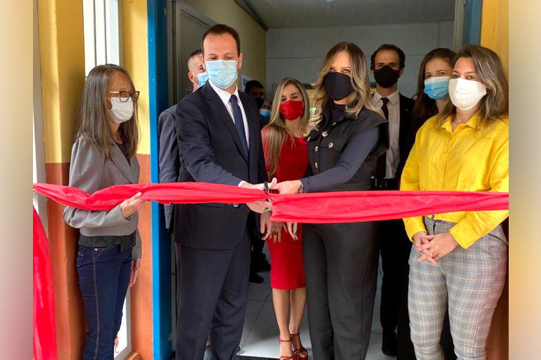 três pessoas, duas mulheres e um homem cortam uma faixa inauguratória na cor vermelha