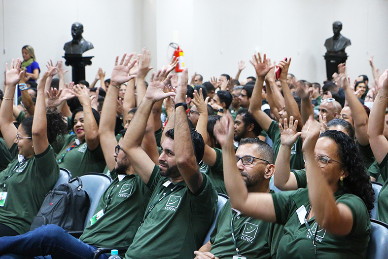 Colaboradores da ONG CETEFE fazem sinal de LIBRAS, balançando as mãos abertas, significando palmas durante evento no salão pleno do TJES.