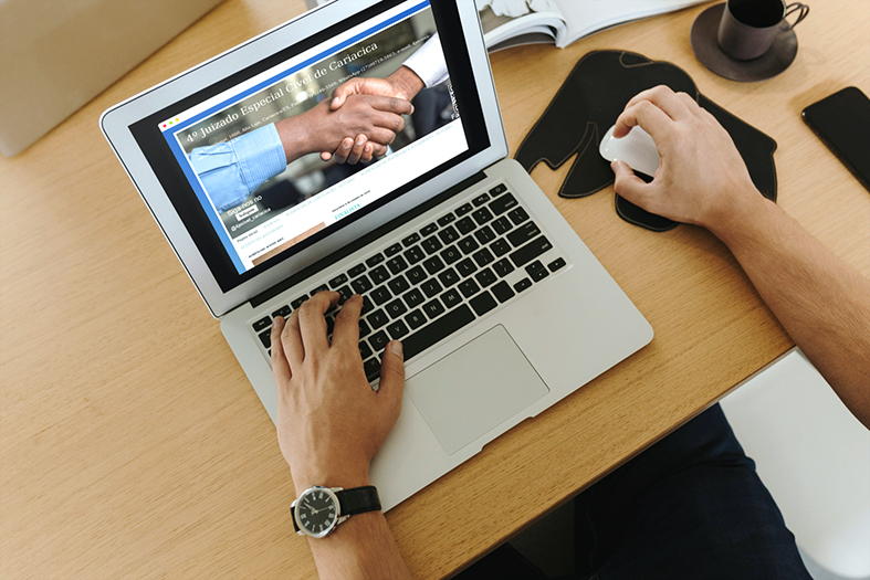 Em uma mesa vemos as mãos de um homem digitando em um laptop. Na tela está projetada a imagem de um blog.