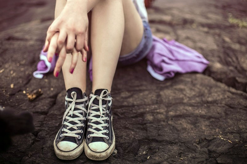 Detalhes das pernas de uma adolescente usando shorts e tênis.