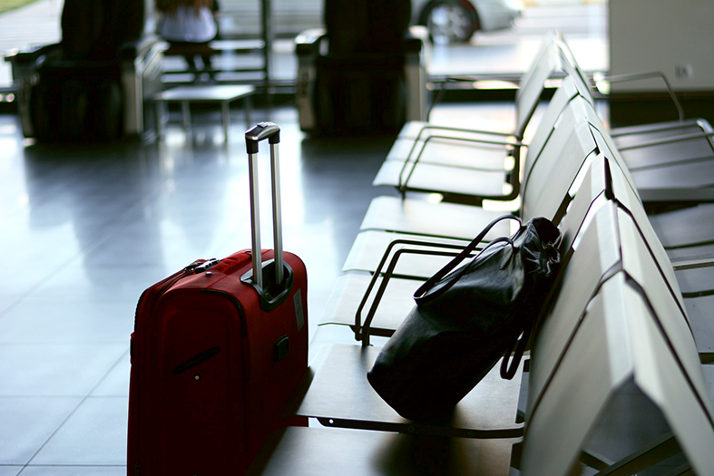 Uma mala vermelha pequena e uma pasta preta repousam em cadeiras de um saguão de embarque de um aeroporto.