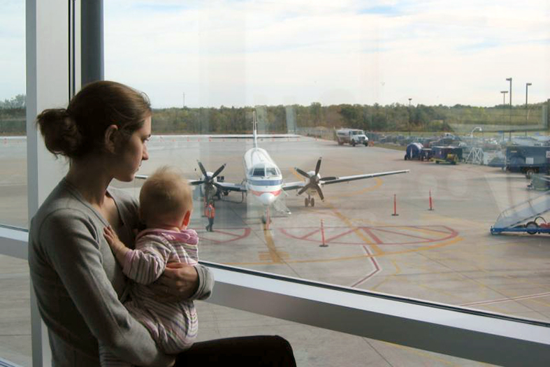 Mãe e bebe de colo observam os aviões em aeroporto.