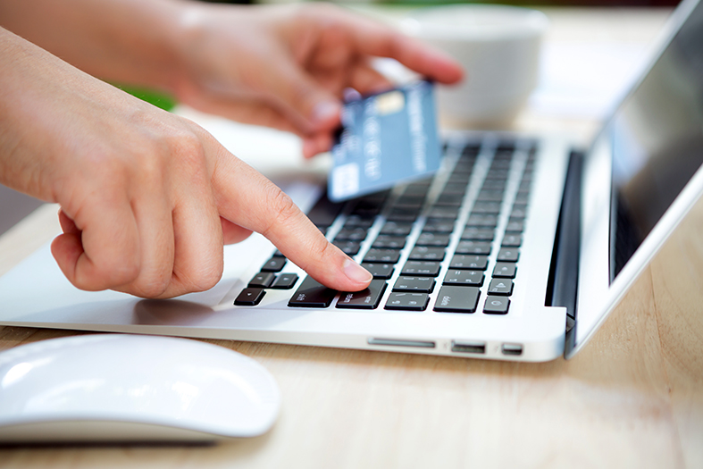 Mãos segurando um cartão de crédito e digitando em um teclado de um laptop