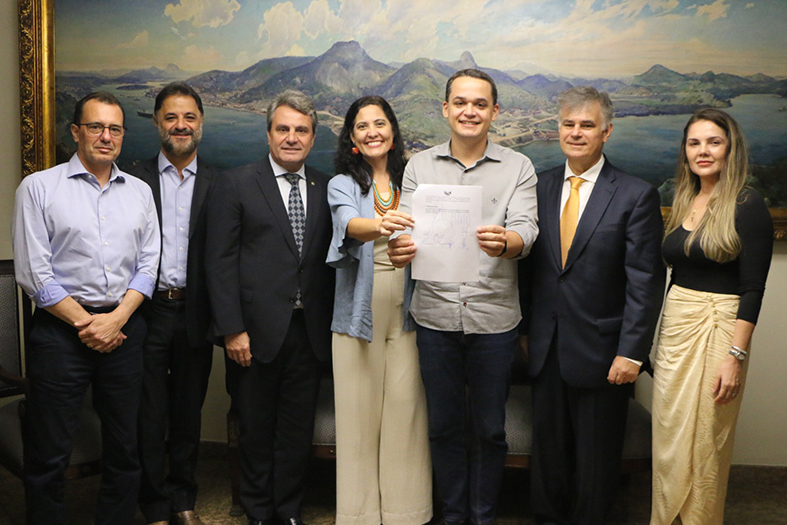 Participantes da reunião reunidos para a foto segurando um papel representando o convênio assinado