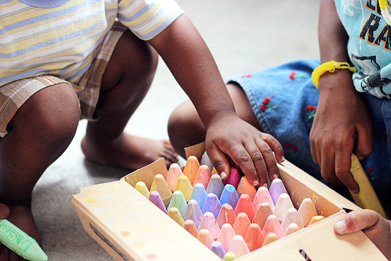 detalhe de duas crianças brincando com lápis de cera coloridos.