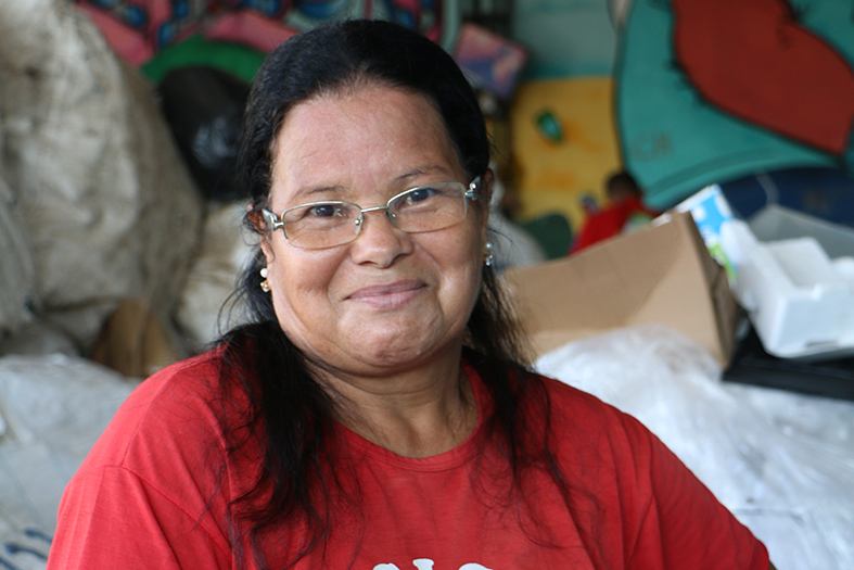 Abigail, mulher de pele parda, com cabelos na cor preta. Ela usa óculos de grau, camiseta na cor vermelha e um adereço de cabelo colorido.