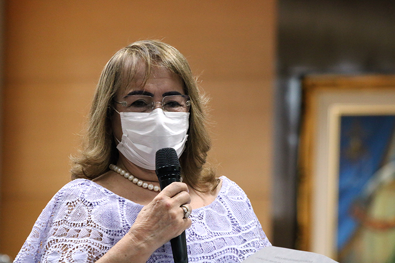 Drª Hermínia Azoury, mulher de pele branca, cabelos tingidos de loiro, usando vestido branco.