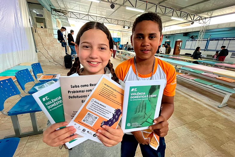 Crianças de ambos os sexos seguram cartilhas informativas.