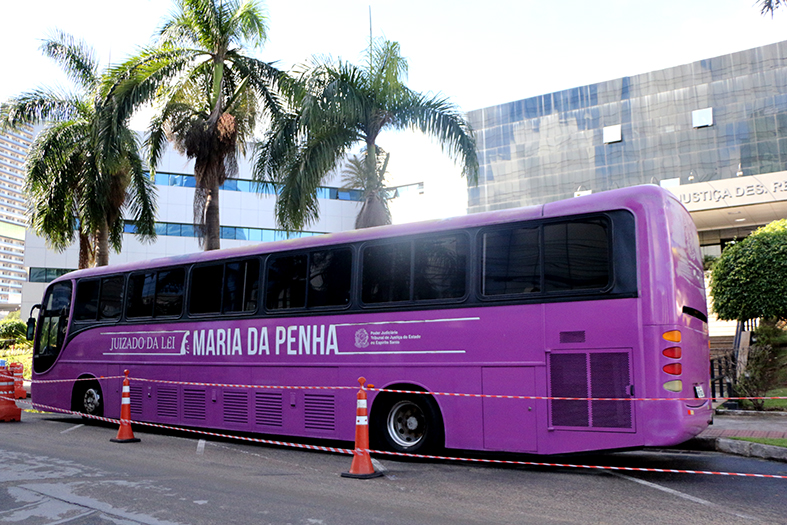 ônibus tipo turismo adesivado em tom de violeta estacionado em frente à sede do TJES
