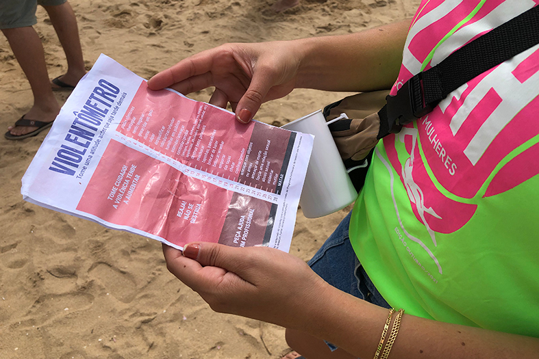 Detalhe de mão de uma mulher segurando um panfleto sobre violência doméstica.