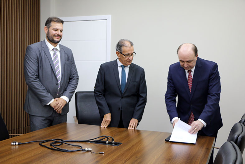 O presidente do TJES, desembargador Samuel Meira Brasil Jr, assina documento na presença do presidente do TRE-ES e do Defensor Público do Espírito Santo.