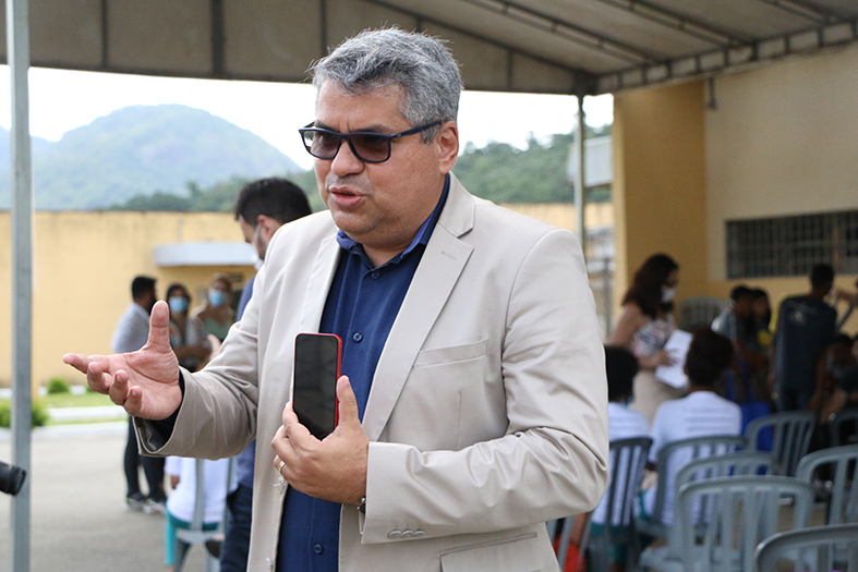 Homem de estatura alta, de pele parda, com cabelos grisalhos dando entrevista. Ele veste terno na cor cinza claro, camisa de botões na cor azul marinho e usa óculos escuros.