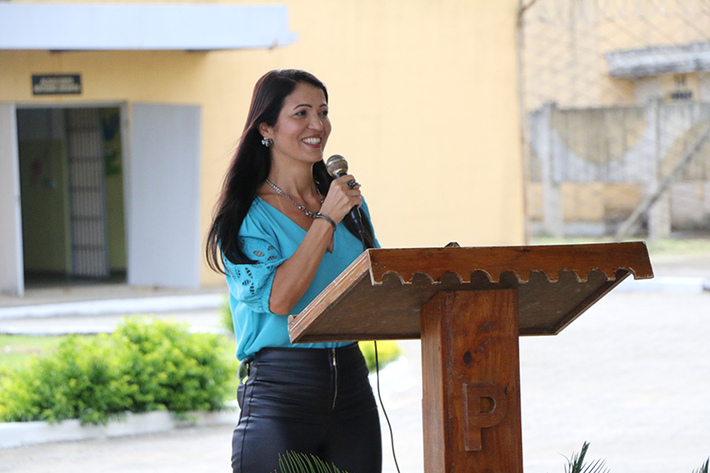 juíza de Direito, Patrícia Faroni fala ao microfone.. Ela é uma mulher de estatura mediana, de pele clara, com cableos longos e na cor preta.