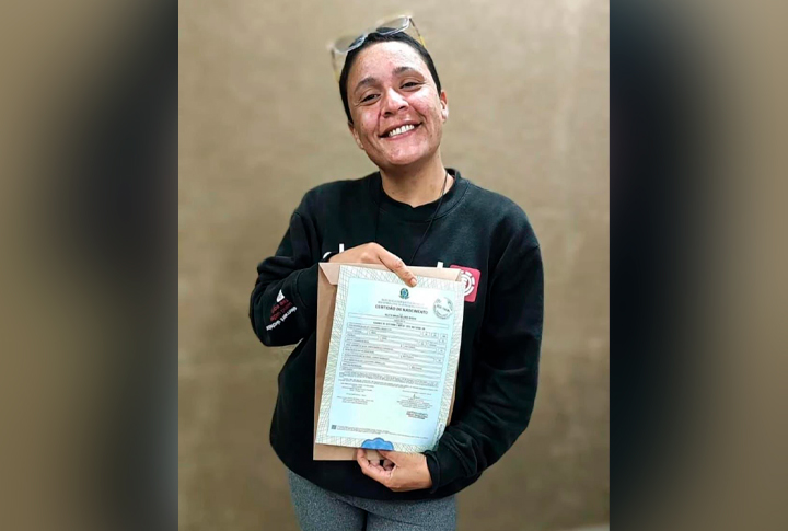 Mulher em situação de rua mostra seu registro civil para a câmera.
