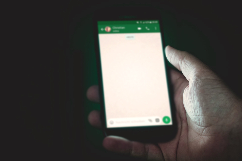 Mão segurando celular cuja tela disponibiliza tela de aplicativo de mensagens.