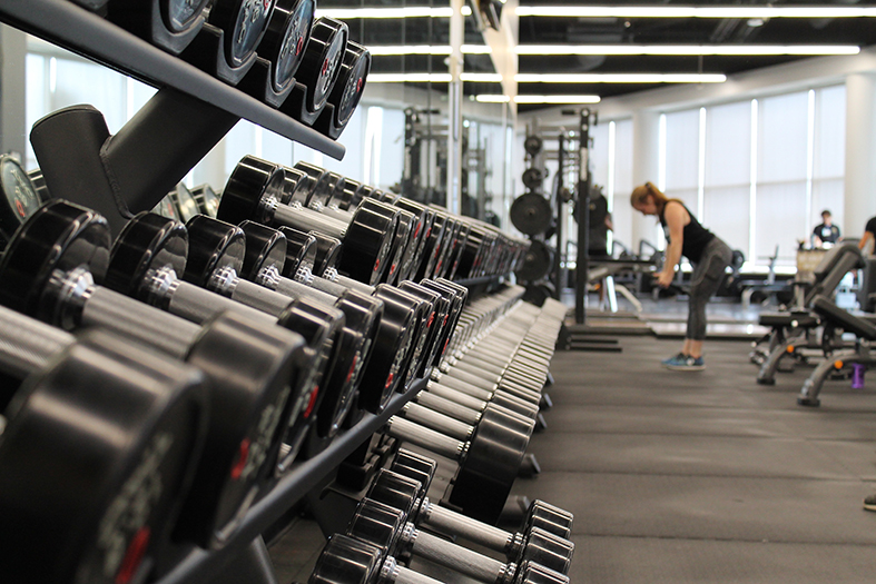 Halteres em primeiro plano em uma foto de pessoas treinando em academia de musculação.