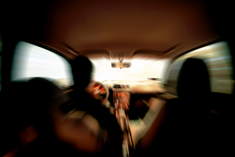 Visão de trás para a frente de um carro onde se vê a parte de trás da cabeça e os braços e mãos no volante.