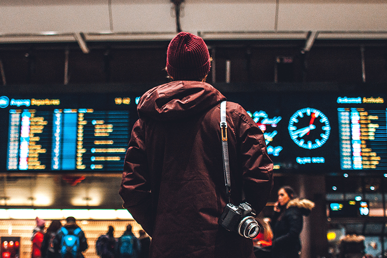 Pessoa de casaco observa vôos no painel eletrônico de um aeroporto.