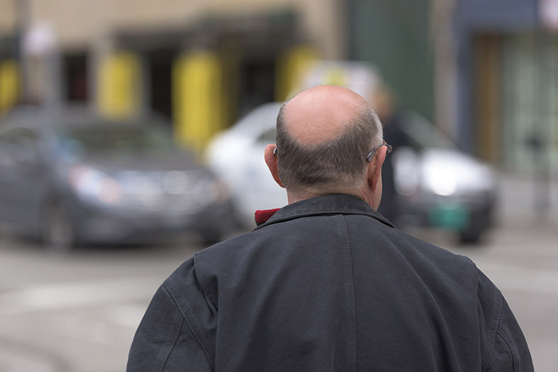 Visão das costas de um idoso calvo andando na rua.