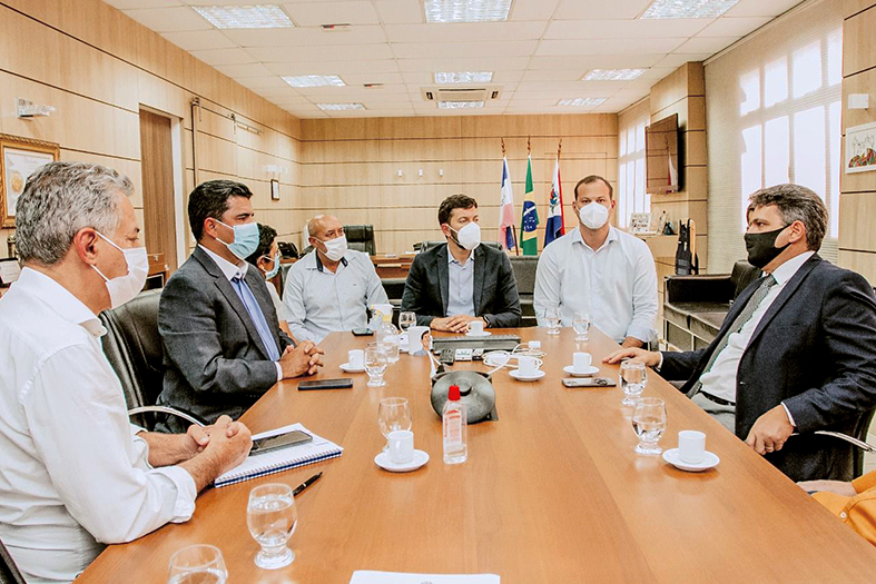 Seis homens de máscara conversam em uma sala de reuniões.